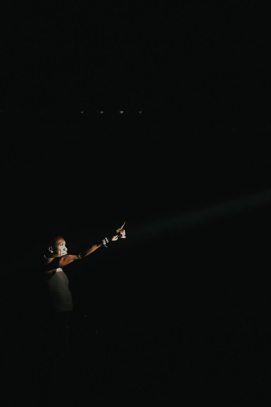 Dramatic image of a performer on stage under a focused spotlight in a dark ambiance.